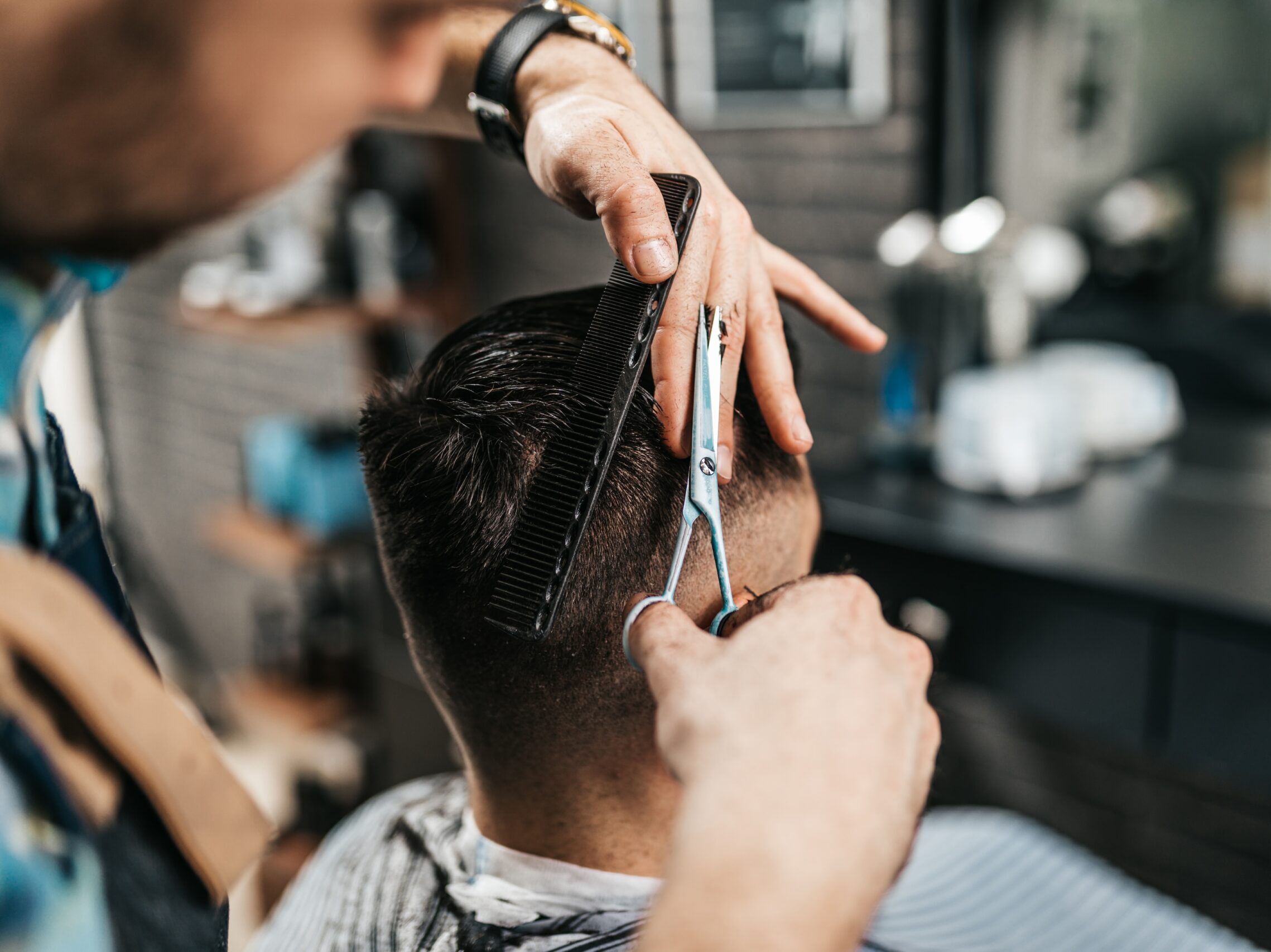 Lähikuva parturista, joka stailaa asiakkaan hiuksia saksilla.